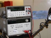 Two measurement instruments displaying electrical values on screens in a lab setting, with red and black leads connected.