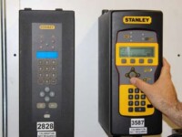 Two Stanley calibration devices with buttons and display screens, one being operated by a hand.