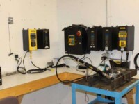 Control panel setup with hydraulic equipment in a workshop, featuring multiple programmable devices and hoses.