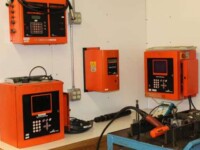 Industrial control panel setup with multiple orange devices and wiring on a white wall in a workshop setting.